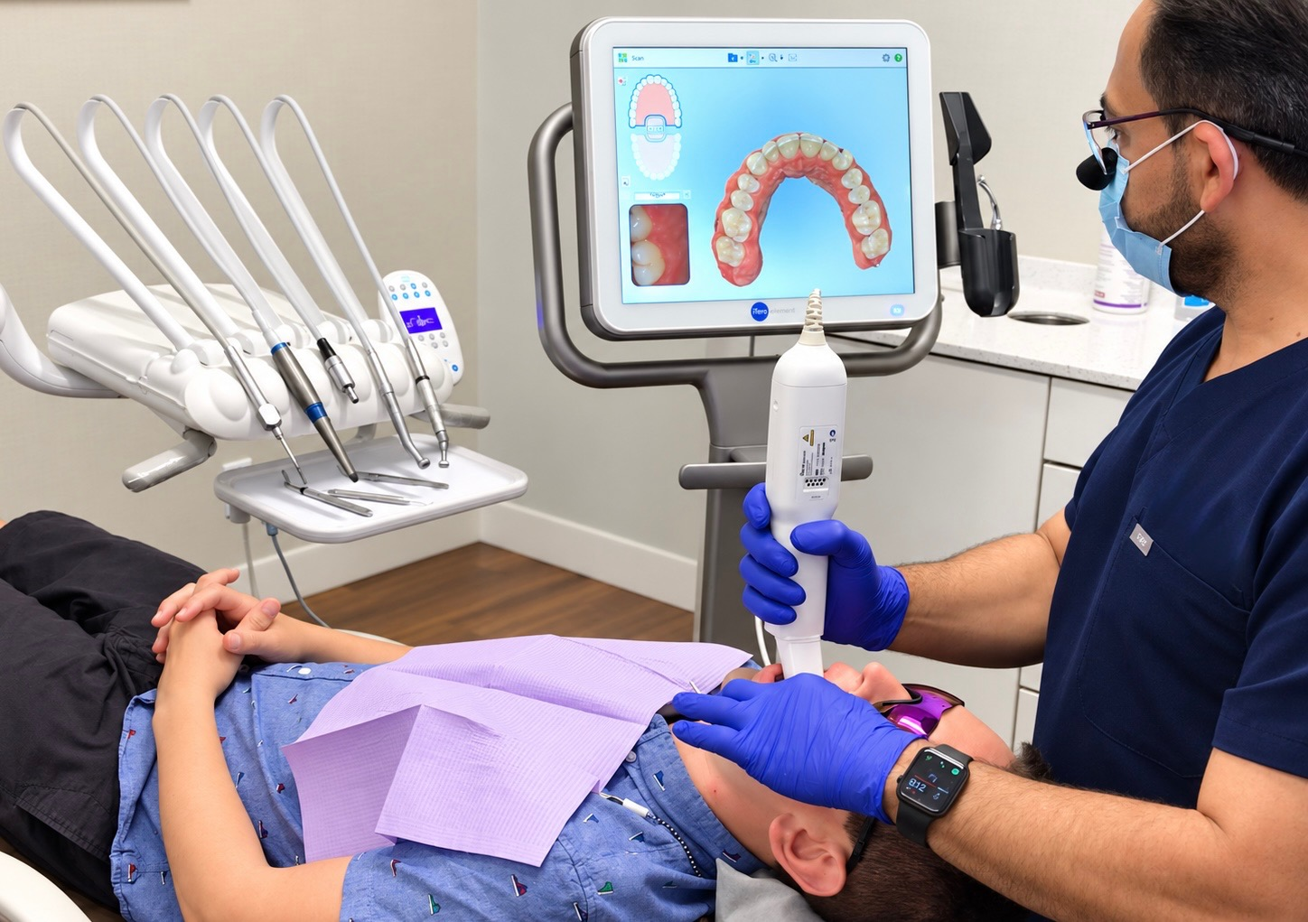 Dentist with a digital intraoral scanner, monitor and reclining patient in a dental treatment room